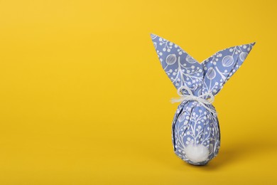 Photo of Easter bunny made of wrapping paper and egg on yellow background. Space for text
