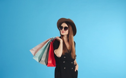 Beautiful young woman with paper shopping bags on light blue background