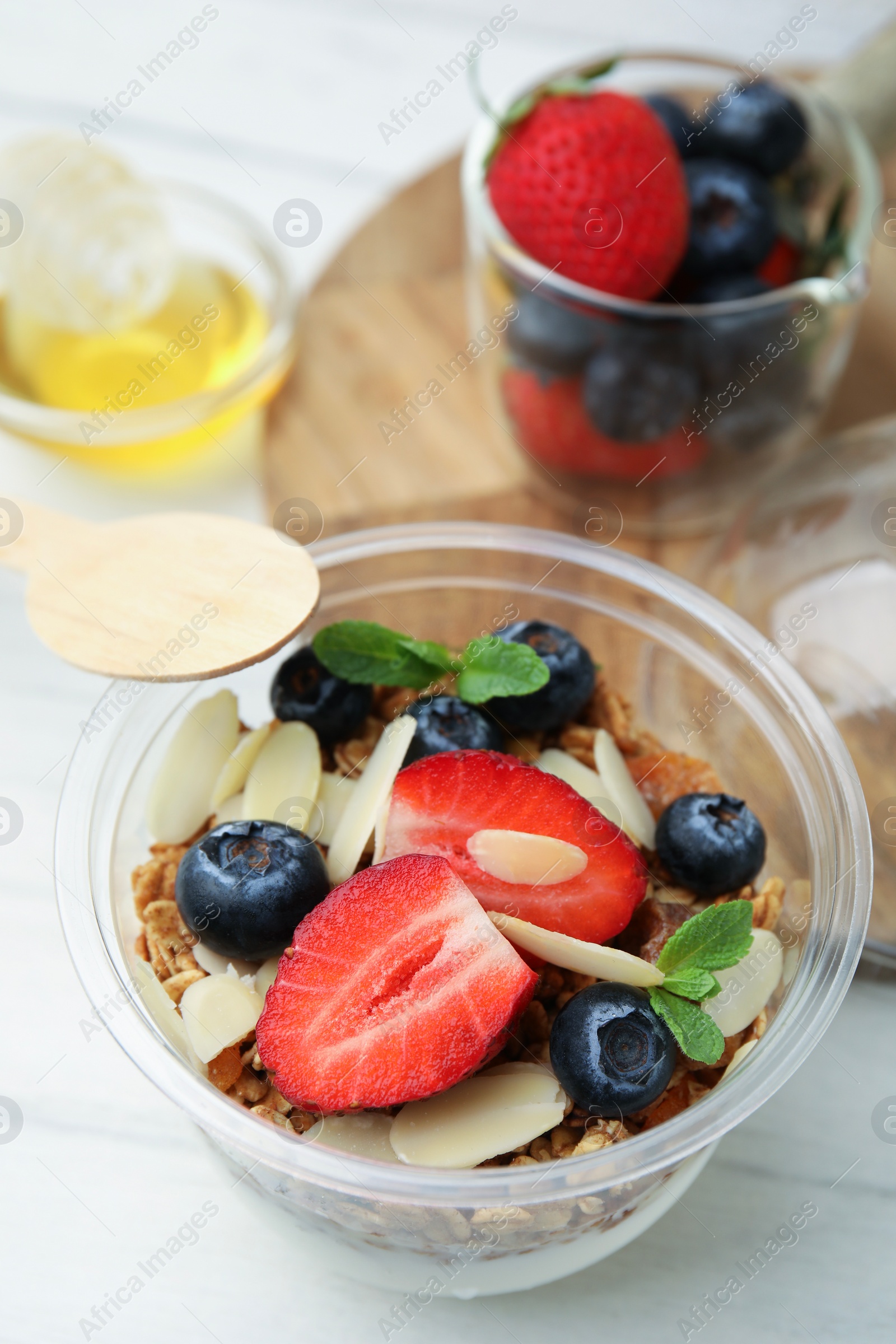 Photo of Tasty granola with berries, yogurt and almond flakes in plastic cup on white table, closeup