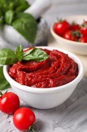 Tasty tomato paste and basil in bowl on light gray table, closeup