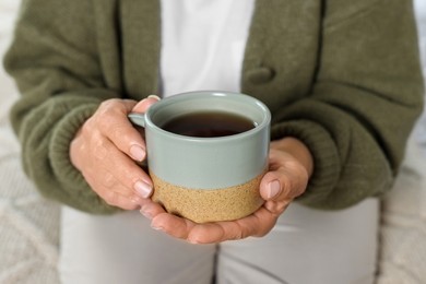 Photo of Elderly woman with cup of hot drink indoors, closeup. Home care service