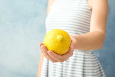 Photo of Woman holding ripe lemon against color background, closeup