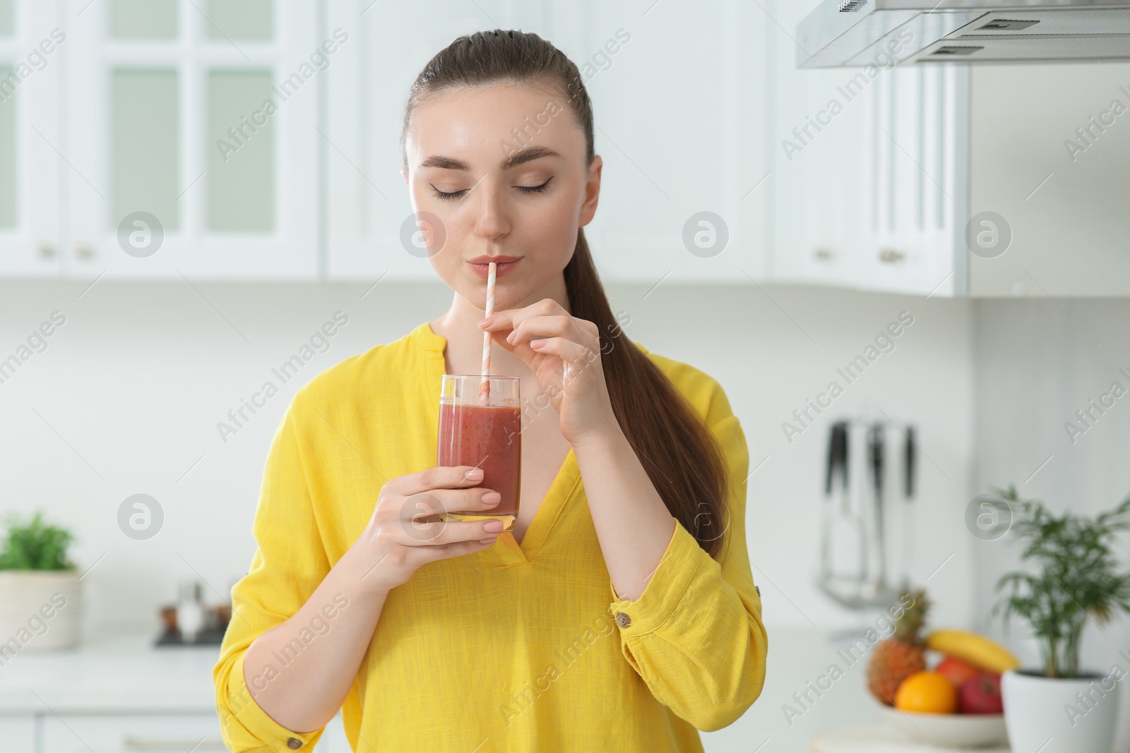 Photo of Beautiful young woman drinking delicious smoothie in kitchen