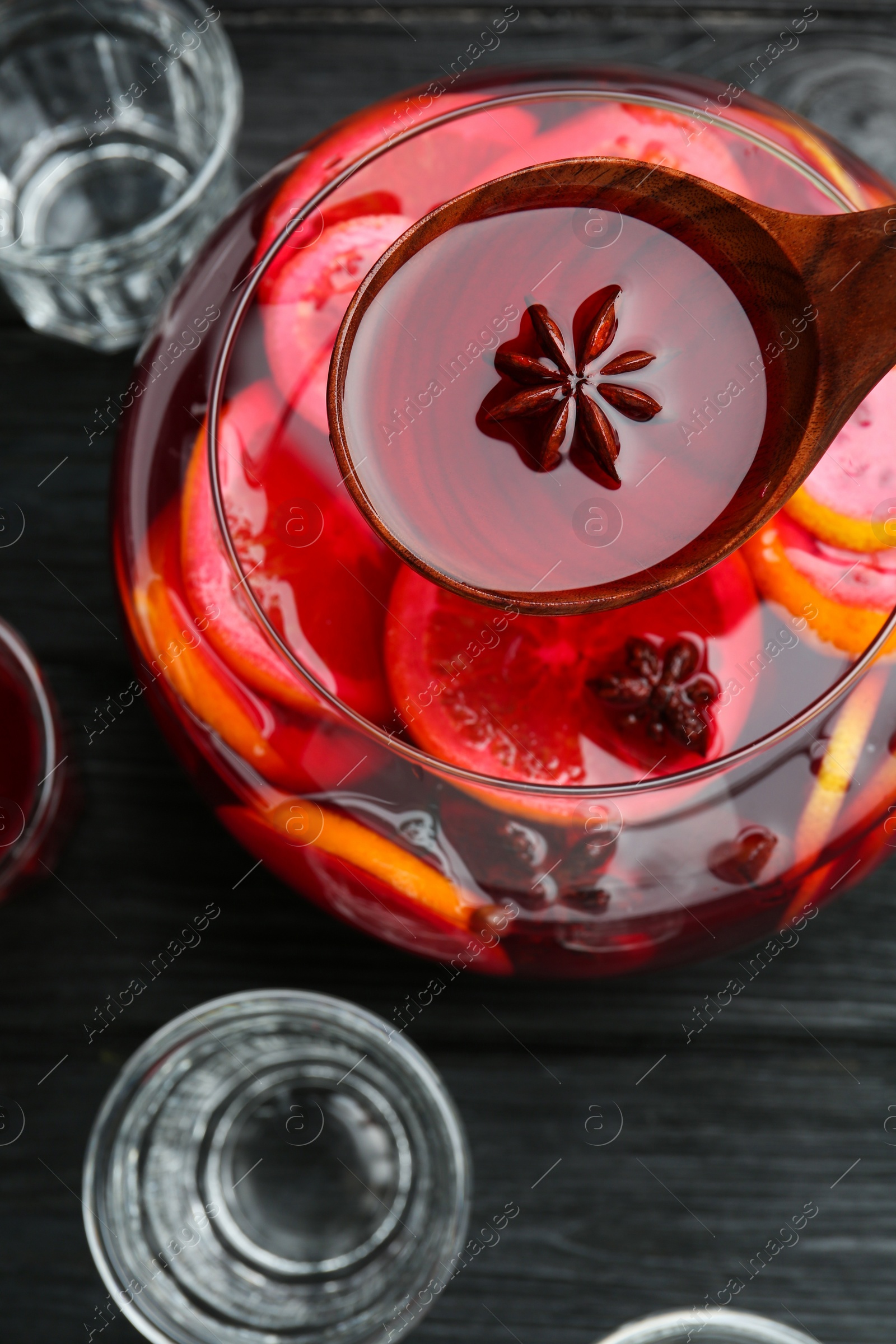 Photo of Ladle of delicious aromatic punch drink over bowl on black wooden table, flat lay