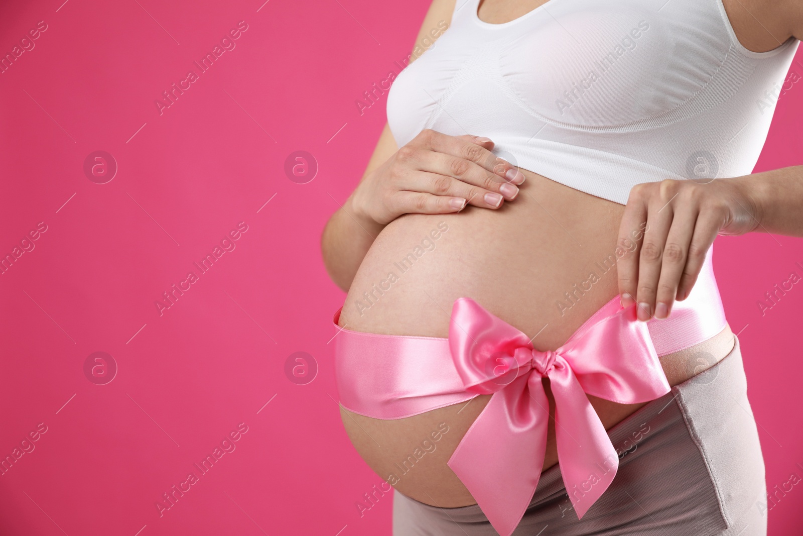 Photo of Young pregnant woman with bow on her belly against pink background, closeup and space for text. Time to give birth