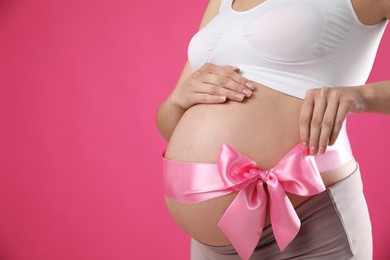 Photo of Young pregnant woman with bow on her belly against pink background, closeup and space for text. Time to give birth