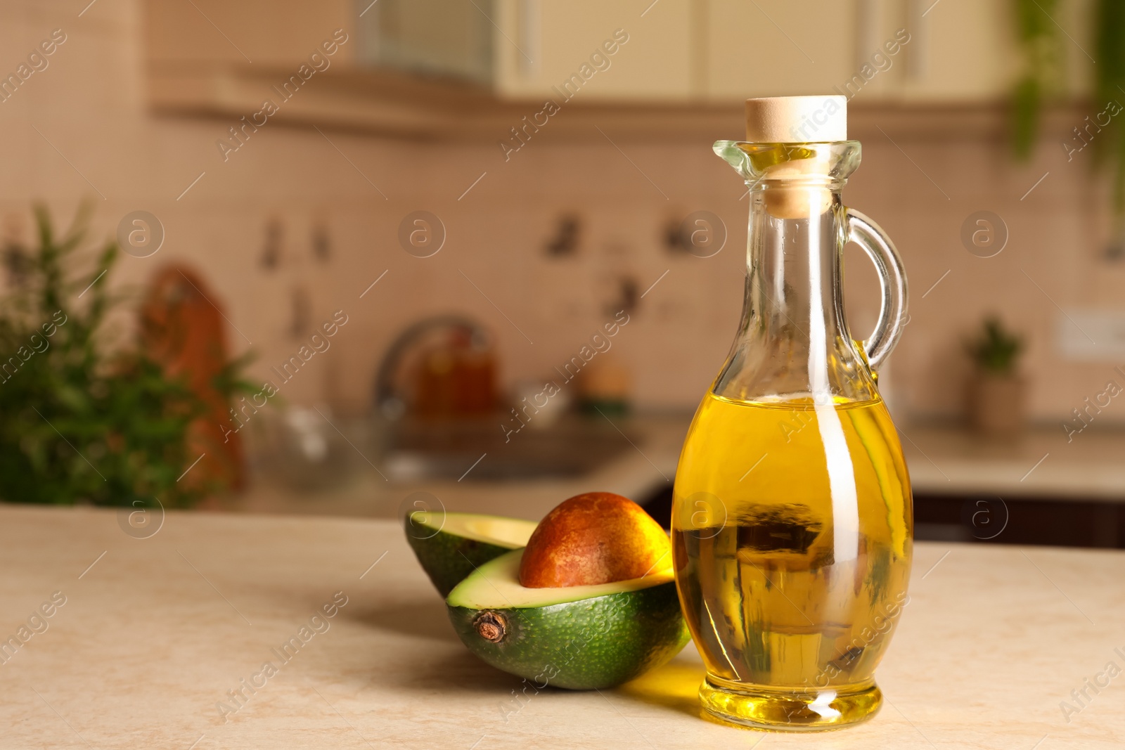 Photo of Fresh avocado and jug of cooking oil on beige table in kitchen, space for text