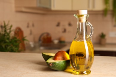 Fresh avocado and jug of cooking oil on beige table in kitchen, space for text