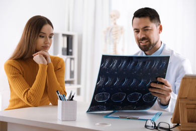 Orthopedist showing X-ray picture to patient at table in clinic