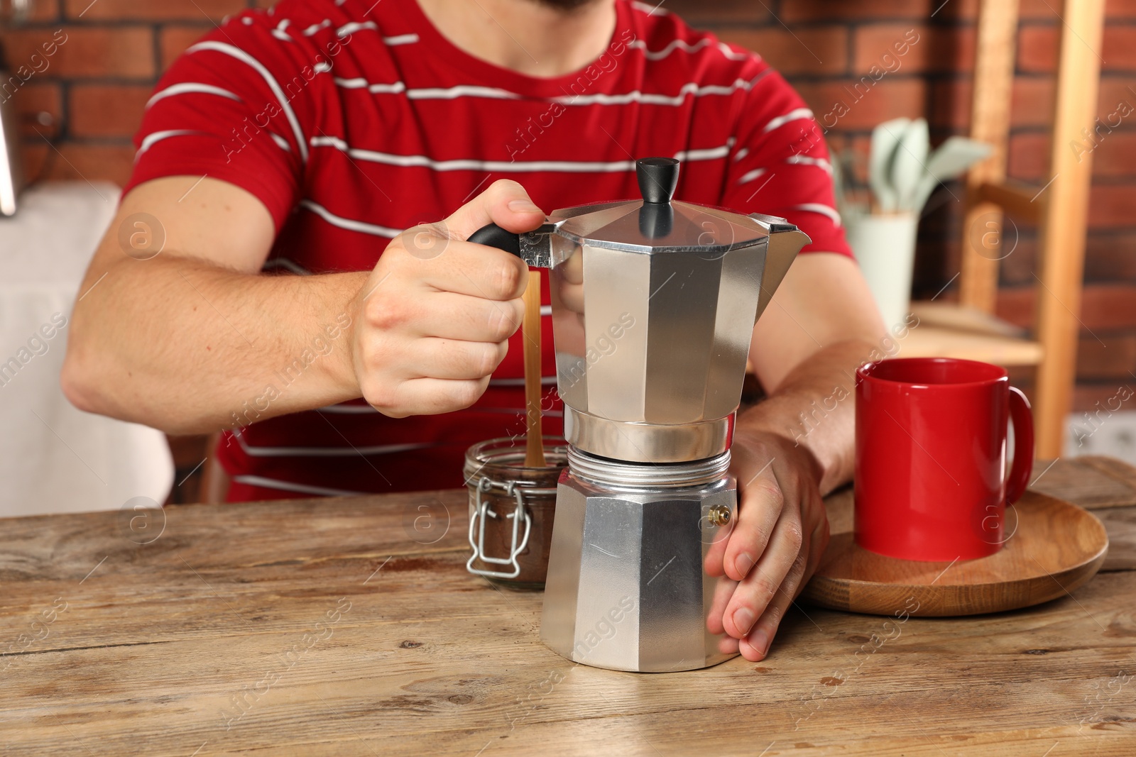 Photo of Brewing coffee. Man with moka pot at wooden table indoors, closeup