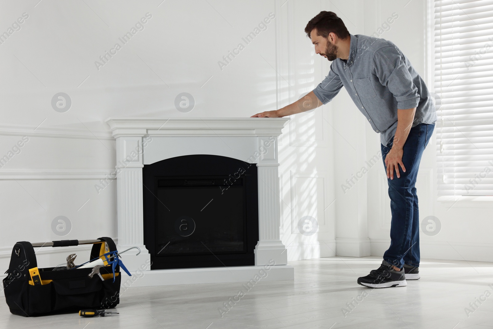 Photo of Man installing electric fireplace near white wall in room