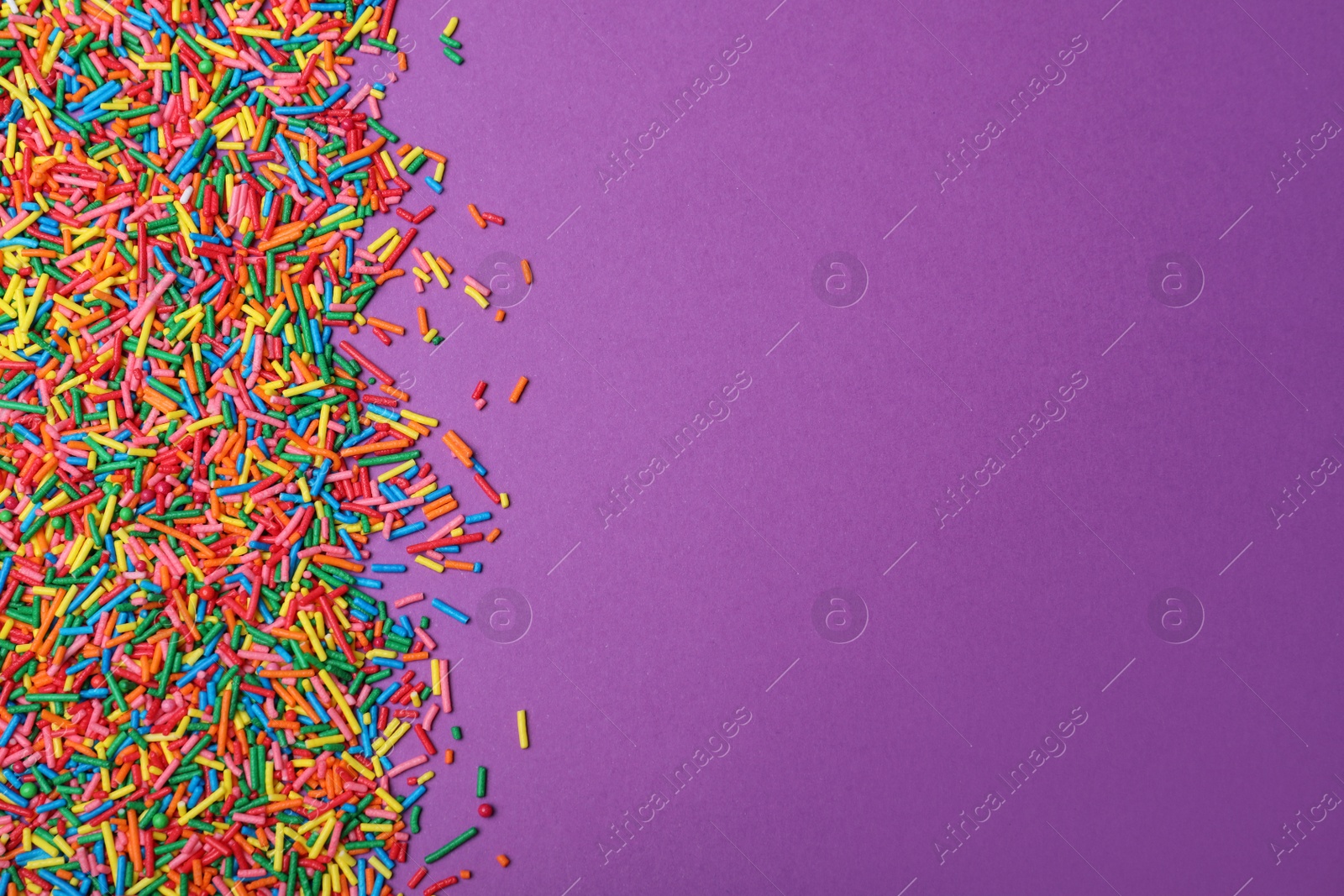 Photo of Colorful sprinkles on purple background, flat lay with space for text. Confectionery decor