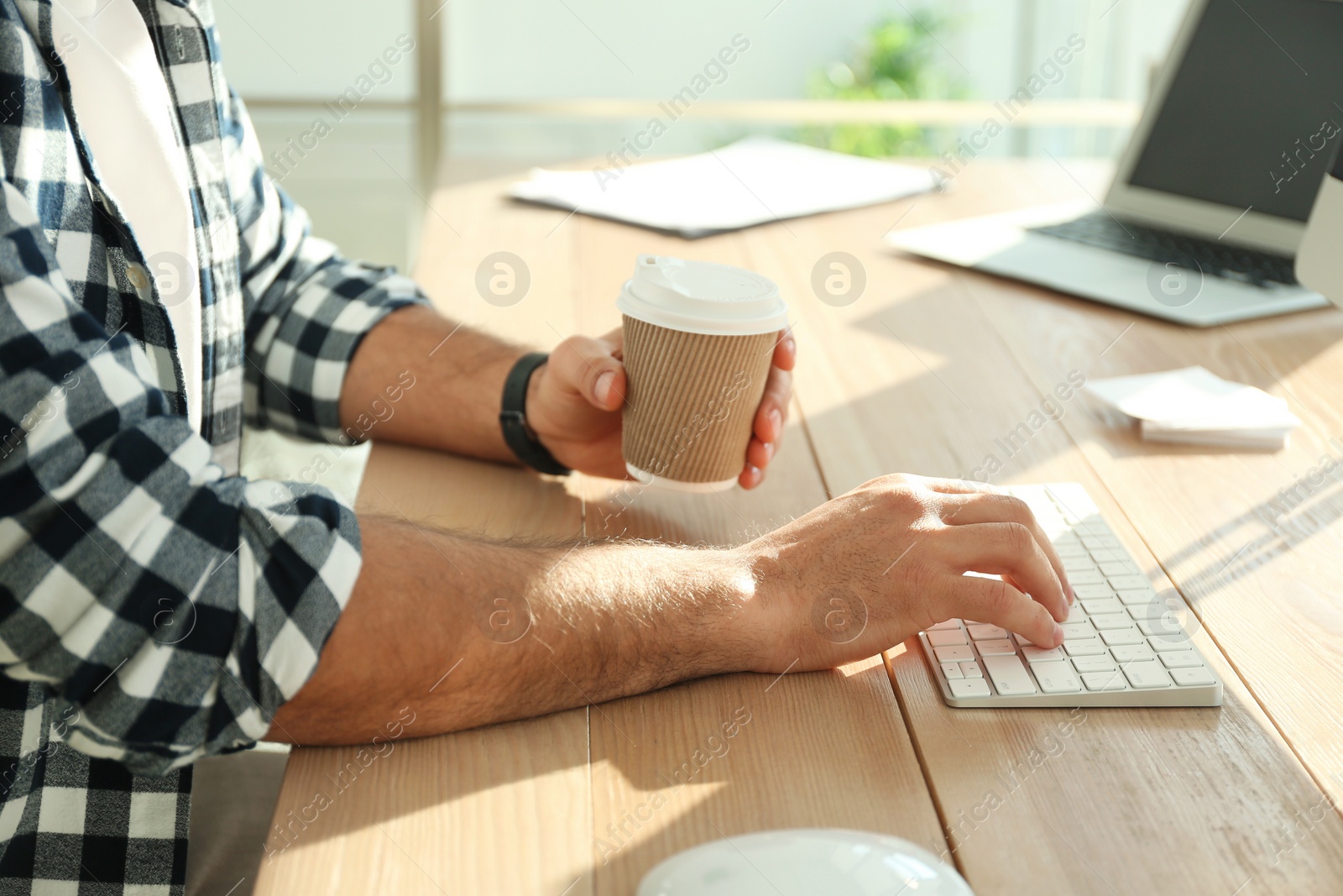 Photo of Freelancer with cup of coffee working on computer at table indoors, closeup