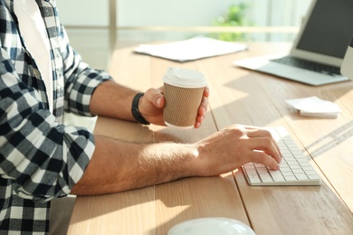 Photo of Freelancer with cup of coffee working on computer at table indoors, closeup