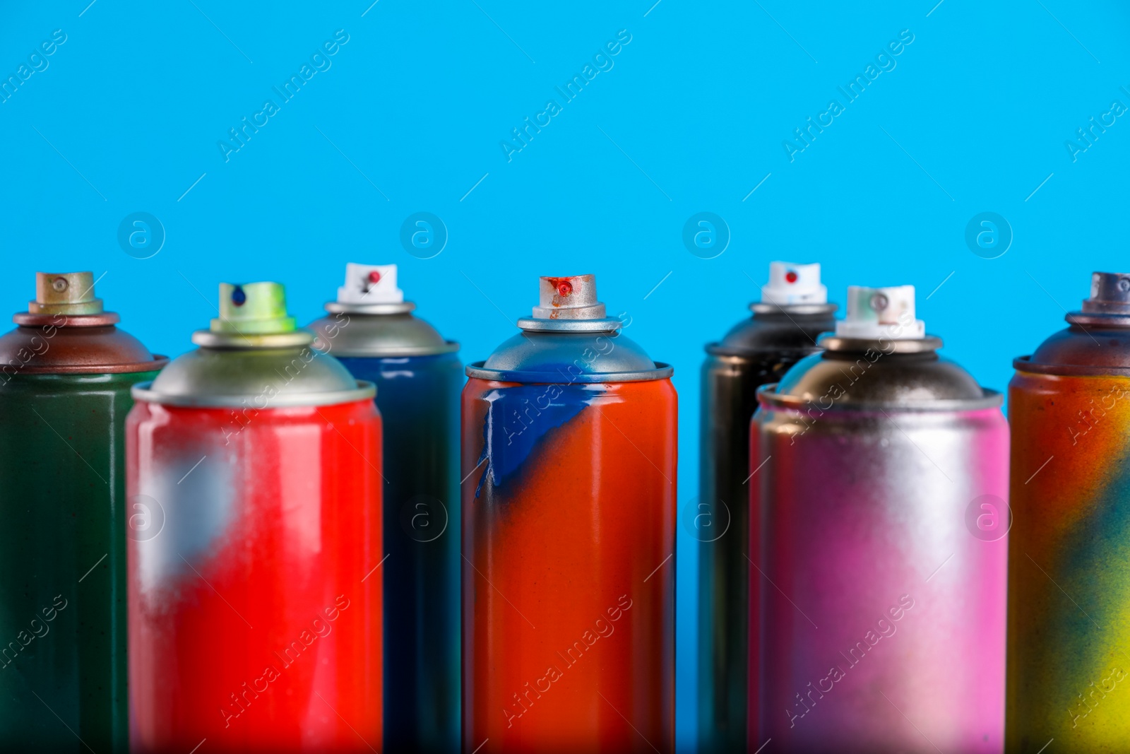 Photo of Used cans of spray paints on light blue background, closeup