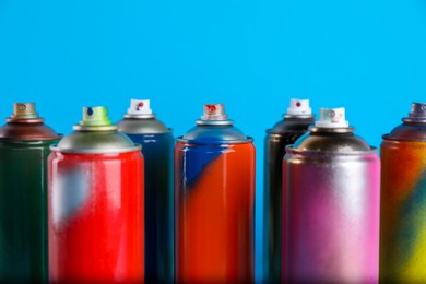 Photo of Used cans of spray paints on light blue background, closeup