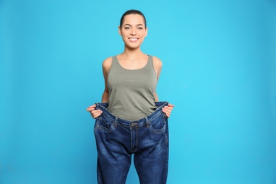 Slim woman in oversized jeans on color background. Weight loss