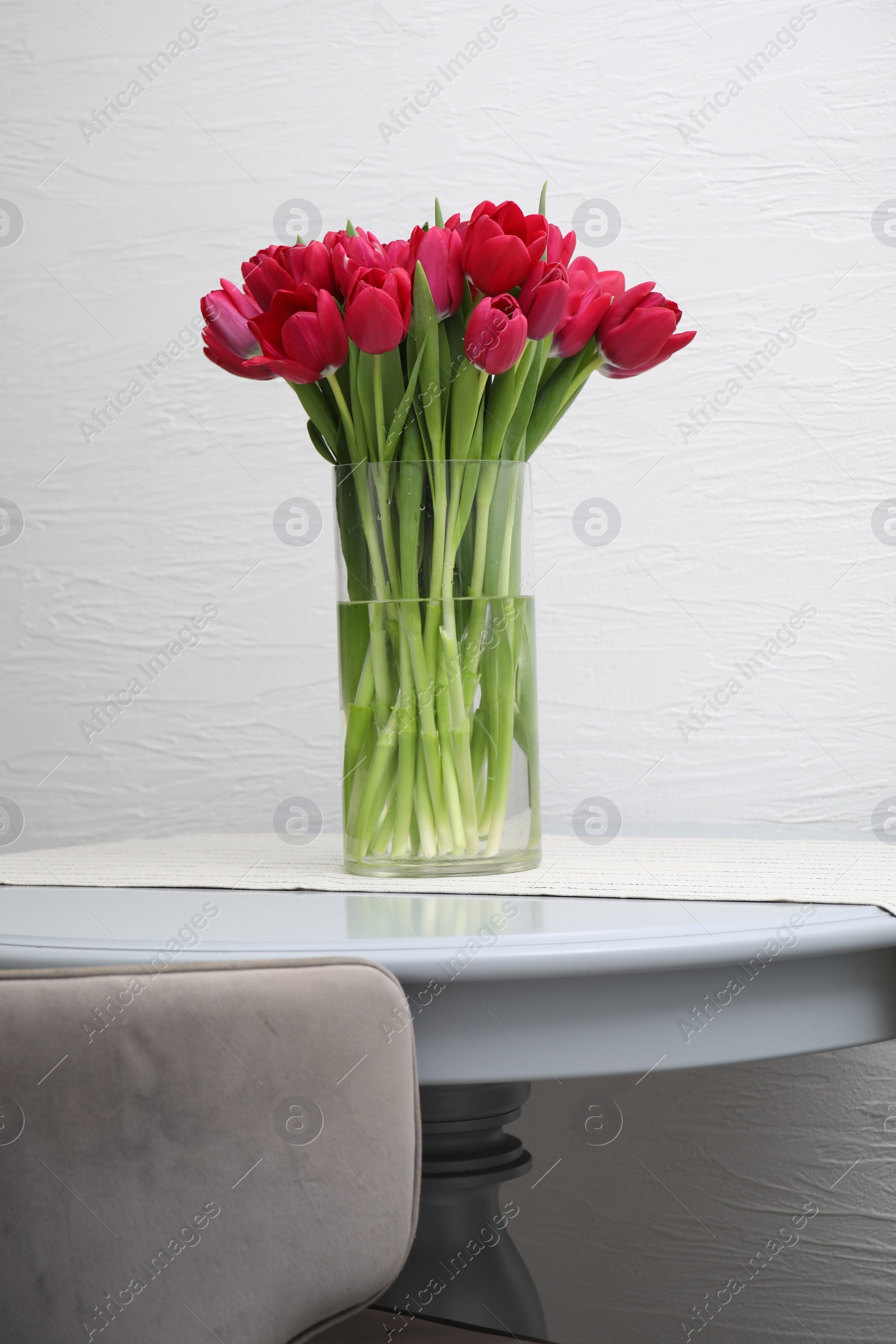 Photo of Bouquet of beautiful tulips in glass vase on table indoors
