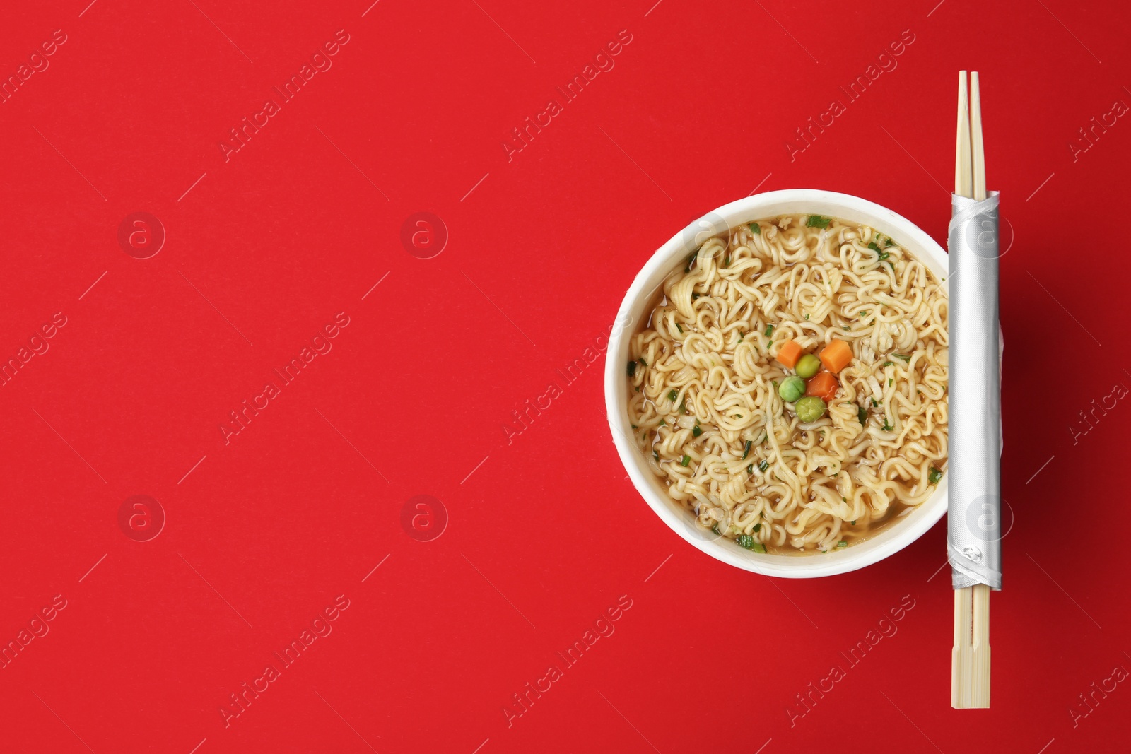 Photo of Cup of cooked instant noodles with chopsticks on color background, top view. Space for text