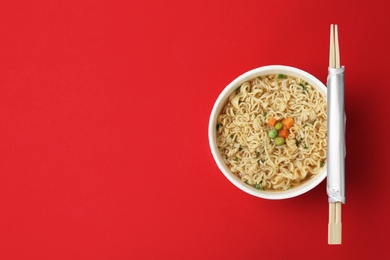 Cup of cooked instant noodles with chopsticks on color background, top view. Space for text