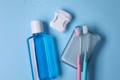 Fresh mouthwash in bottle, toothbrushes and dental floss on light blue background, flat lay