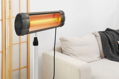 Photo of Functional electric infrared heater near sofa indoors