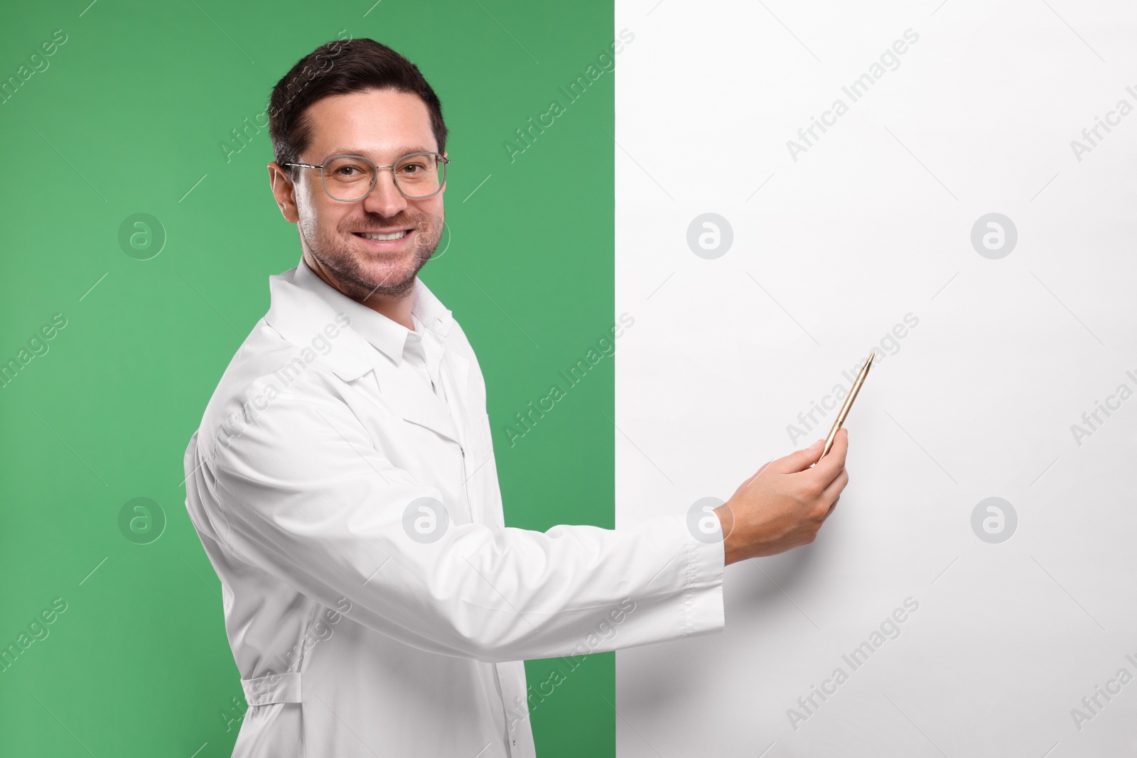 Photo of Ophthalmologist pointing at blank banner on green background, space for text