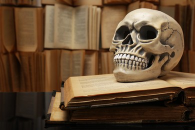 Photo of Human skull and old books on mirror table. Space for text