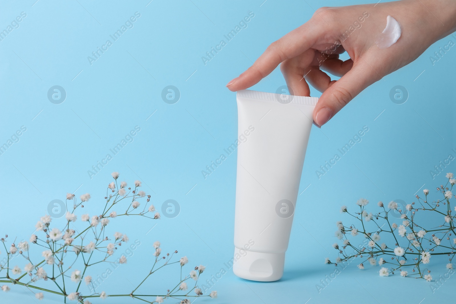 Photo of Woman with tube of cream and flowers on light blue background, closeup