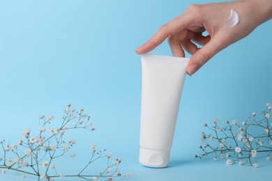 Photo of Woman with tube of cream and flowers on light blue background, closeup