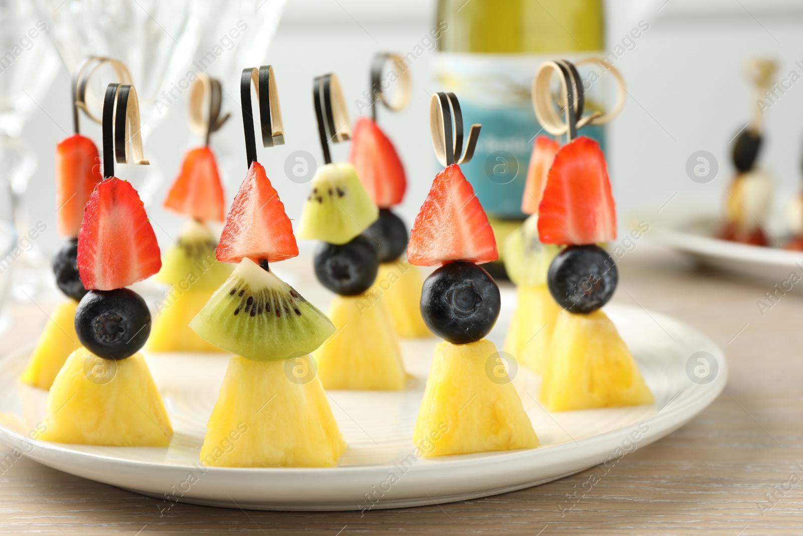 Photo of Tasty canapes with pineapple, kiwi and berries on light wooden table, closeup