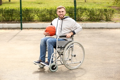 Happy man in wheelchair with ball on sports ground