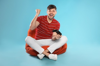 Emotional man playing video games with controller on color background