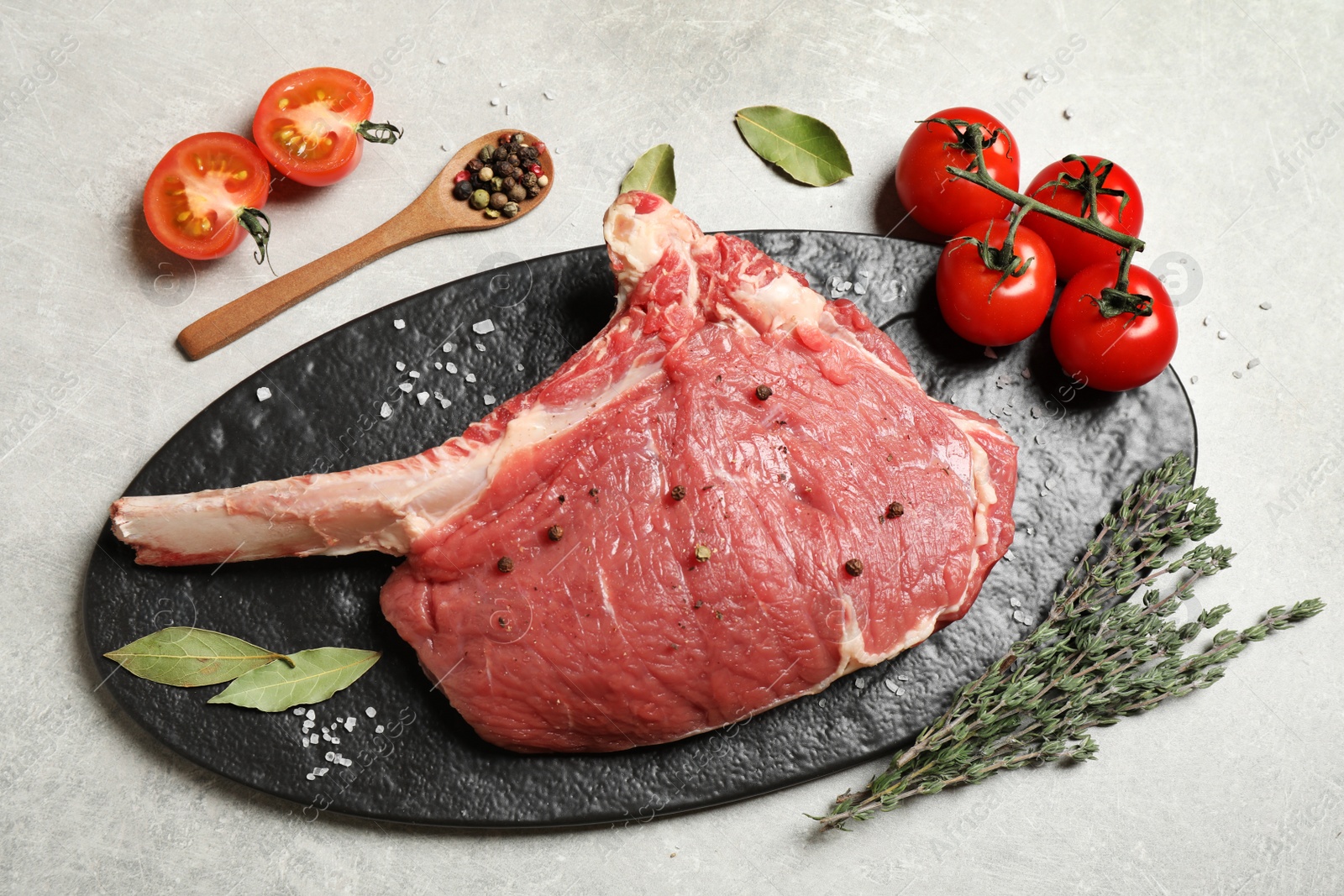 Photo of Raw rib with herbs, spices and tomatoes on grey table, flat lay