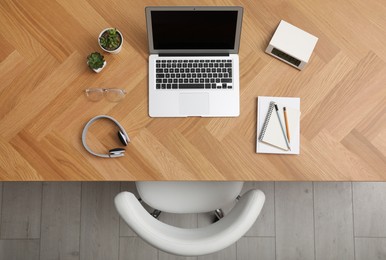 Photo of Wooden table with modern laptop near office chair indoors, top view. Comfortable workplace