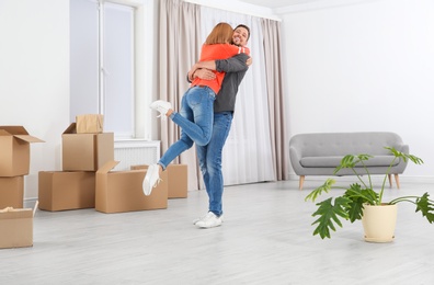 Photo of Happy couple hugging near moving boxes in their new house