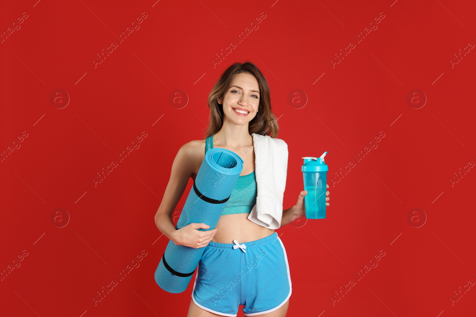 Photo of Beautiful woman with yoga mat, towel and shaker on red background