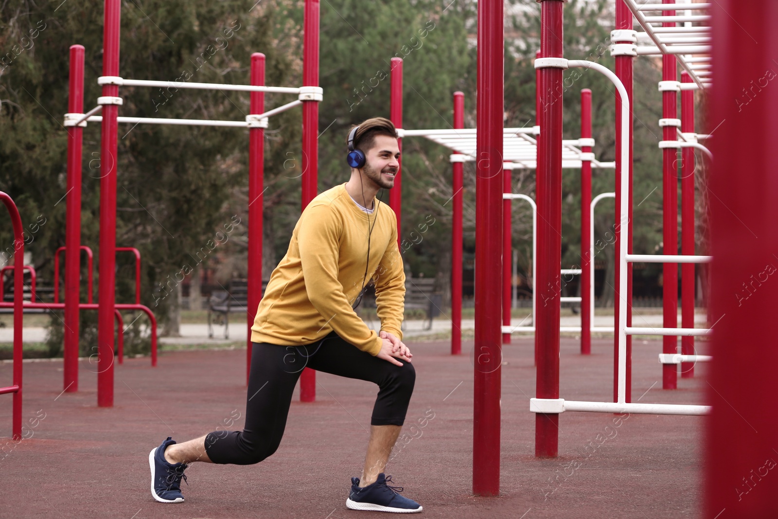 Photo of Young man with headphones listening to music and exercising on sports ground