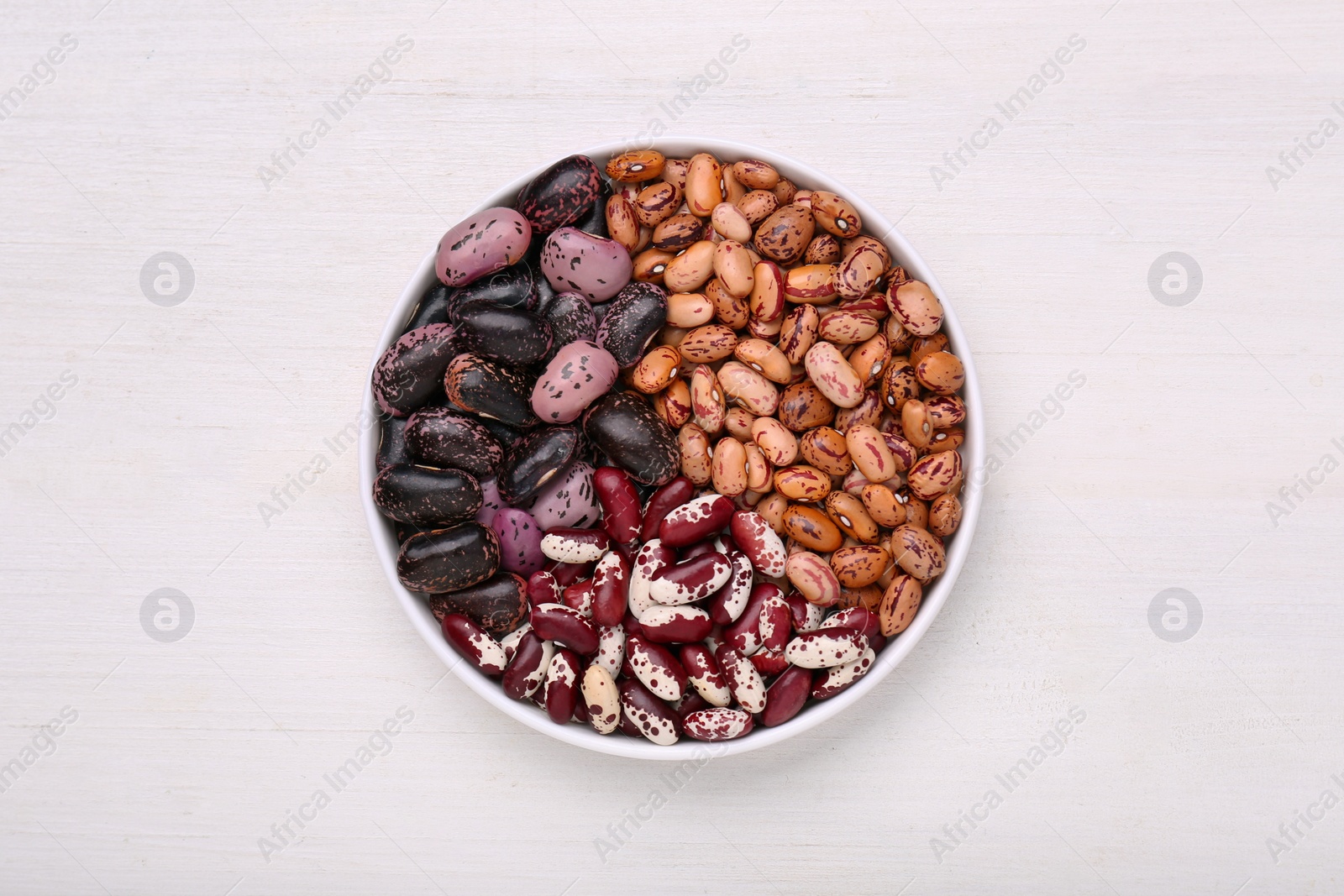 Photo of Bowl with different types of beans on white wooden table, top view