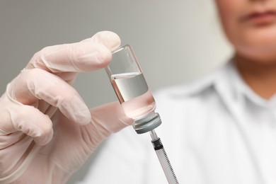 Photo of Doctor filling syringe with medication from glass vial on grey background, closeup