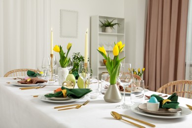 Photo of Festive Easter table setting with painted eggs, burning candles and yellow tulips indoors