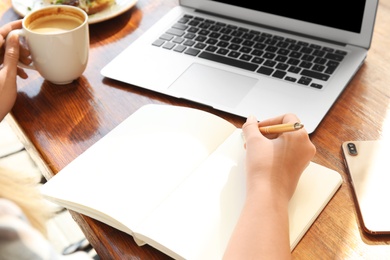 Photo of Woman writing blog content in notebook at table, closeup