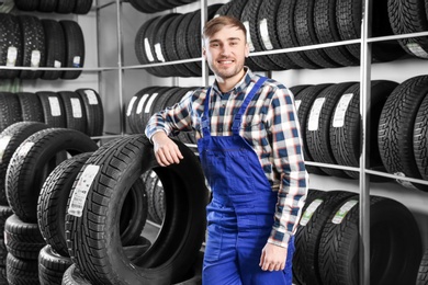 Young male mechanic with car tires in automobile service center