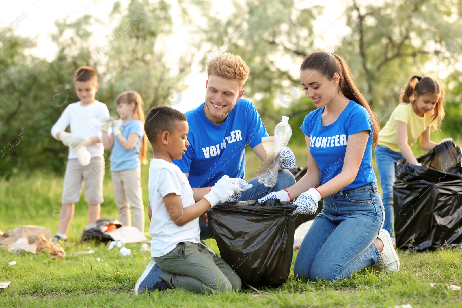 Photo of Little African-American boy collecting trash with volunteers in park