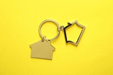 Photo of Metallic keychains in shape of houses on yellow background, top view