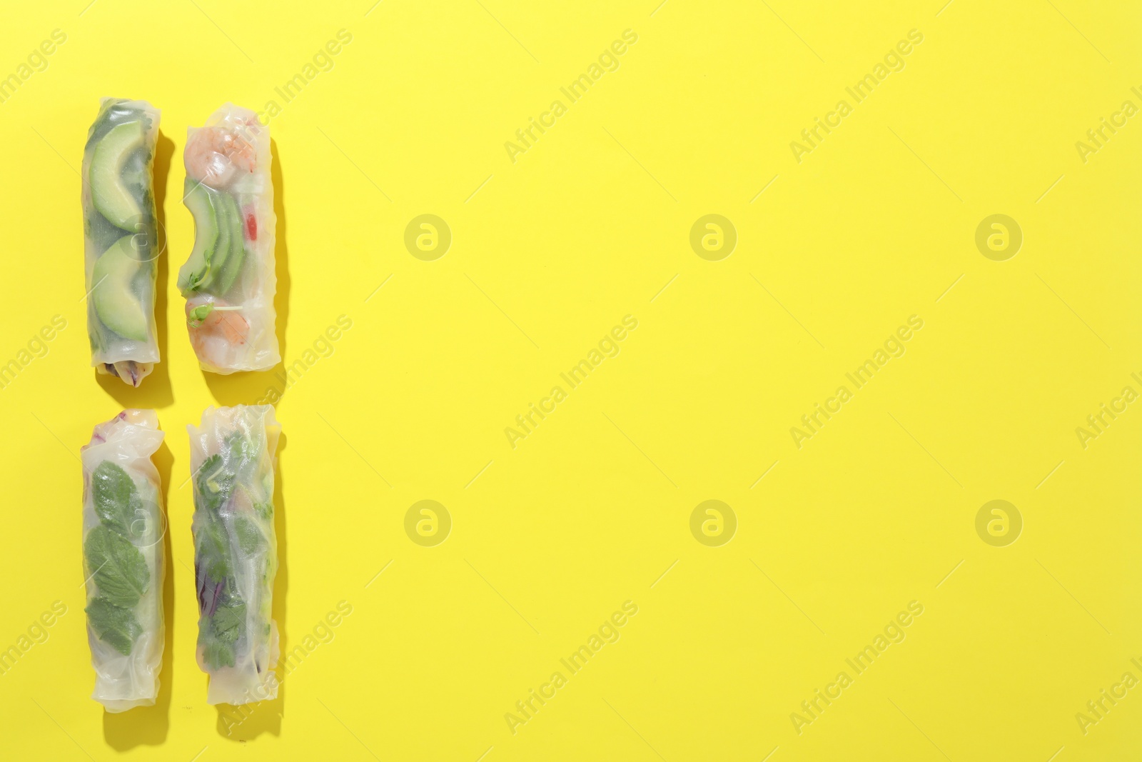 Photo of Delicious spring rolls wrapped in rice paper on yellow background, flat lay. Space for text