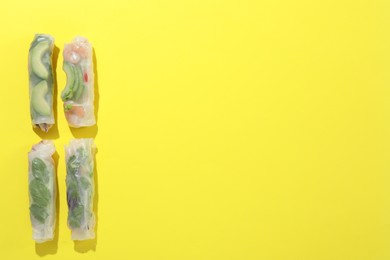 Photo of Delicious spring rolls wrapped in rice paper on yellow background, flat lay. Space for text