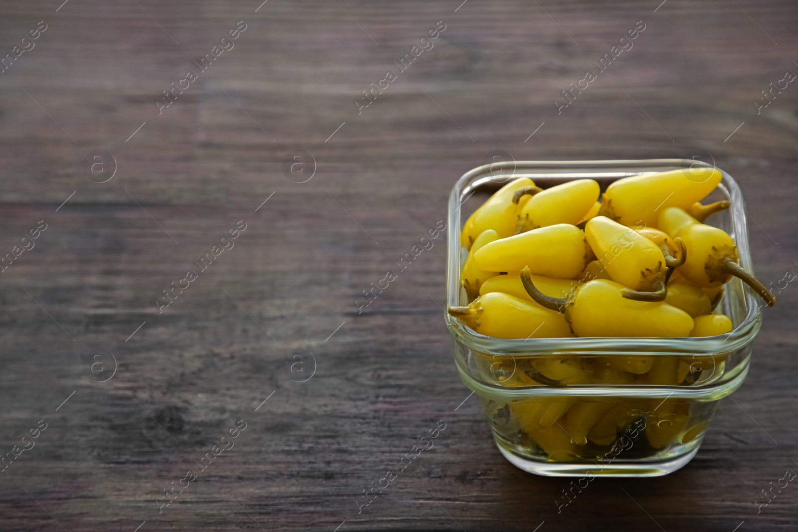 Photo of Glass bowl of pickled yellow jalapeno peppers on wooden table. Space for text