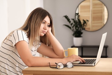 Photo of Sleepy young woman working with laptop at wooden table indoors