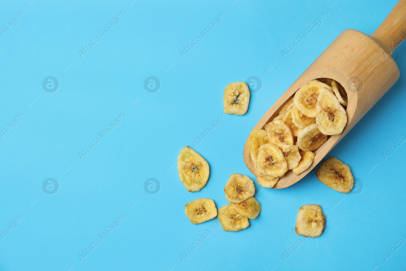 Photo of Wooden scoop with banana slices on color background, top view with space for text. Dried fruit as healthy snack